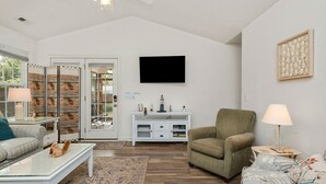 Ein Wohnzimmer mit Sofa, Sessel, Couchtisch und einem an der Wand befestigten Fernseher.