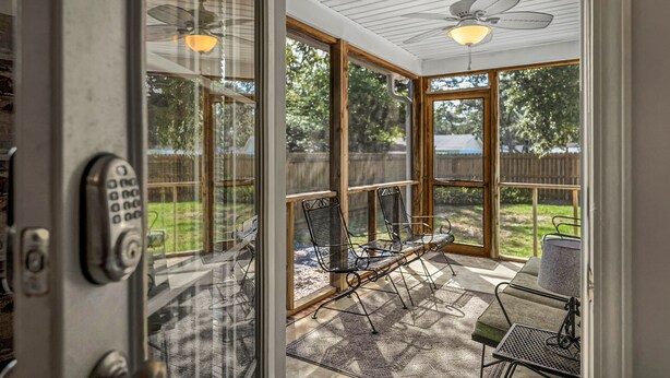 Ein Wintergarten mit Glastür, Deckenventilator und Gartenmöbeln.