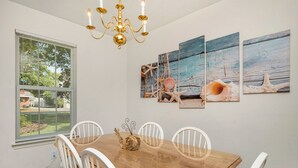 Ein Essbereich mit Holztisch, weißen Stühlen, einer Chandelierleuchtre und drei an der Wand befestigten Bildern.