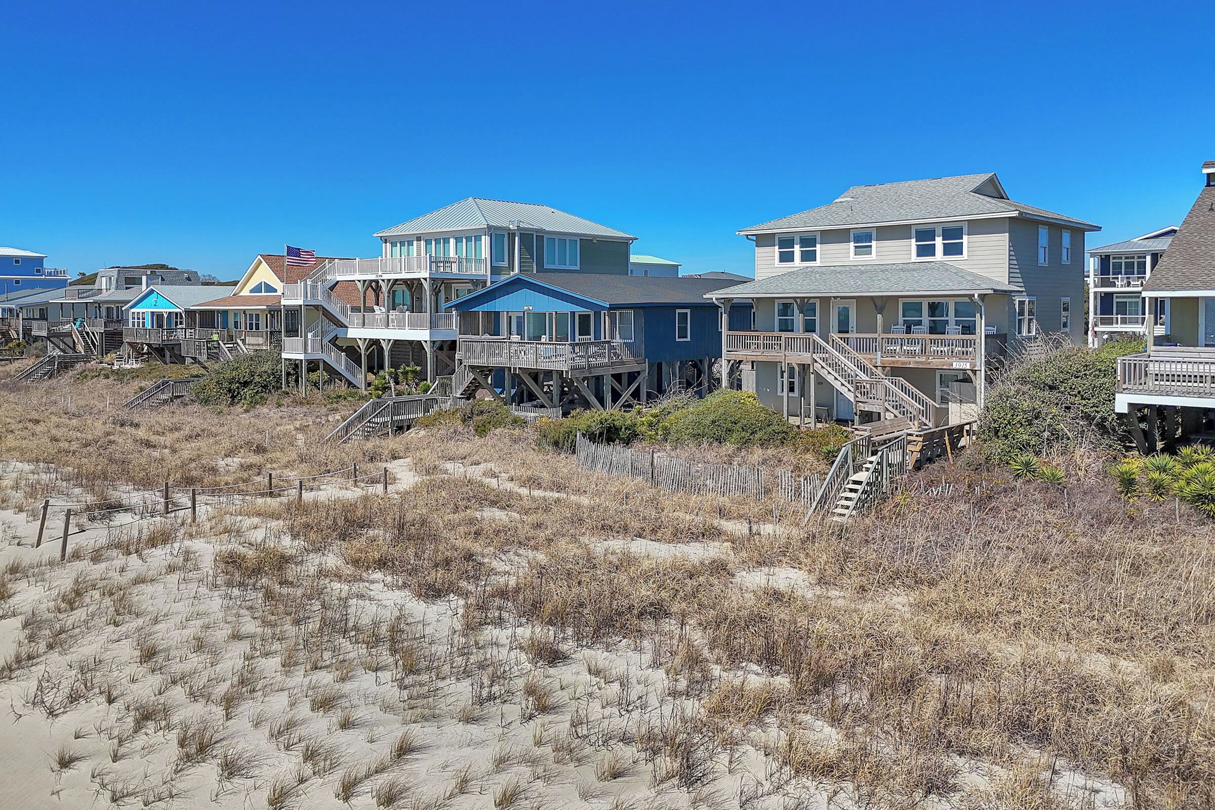 A beachfront property with multiple houses connected by walkways, featuring outdoor decks and a sandy beach area.
