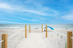 Una spiaggia sabbiosa con pali di legno e corde che conducono all'oceano.
