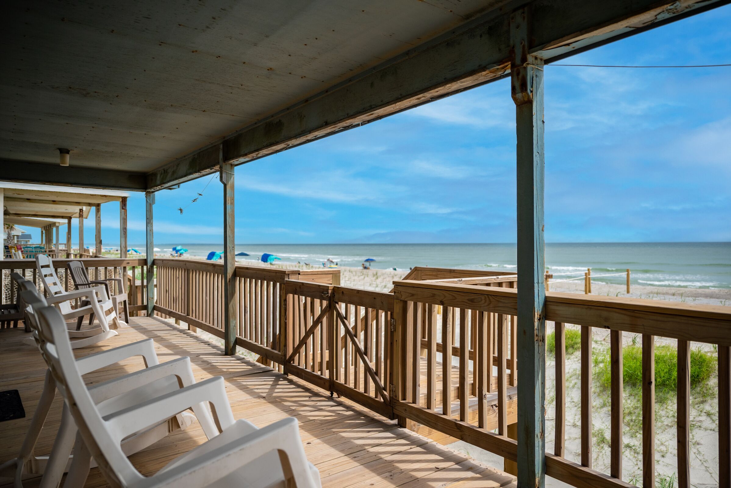 A wooden deck with beach chairs overlooking a sandy beach and ocean.