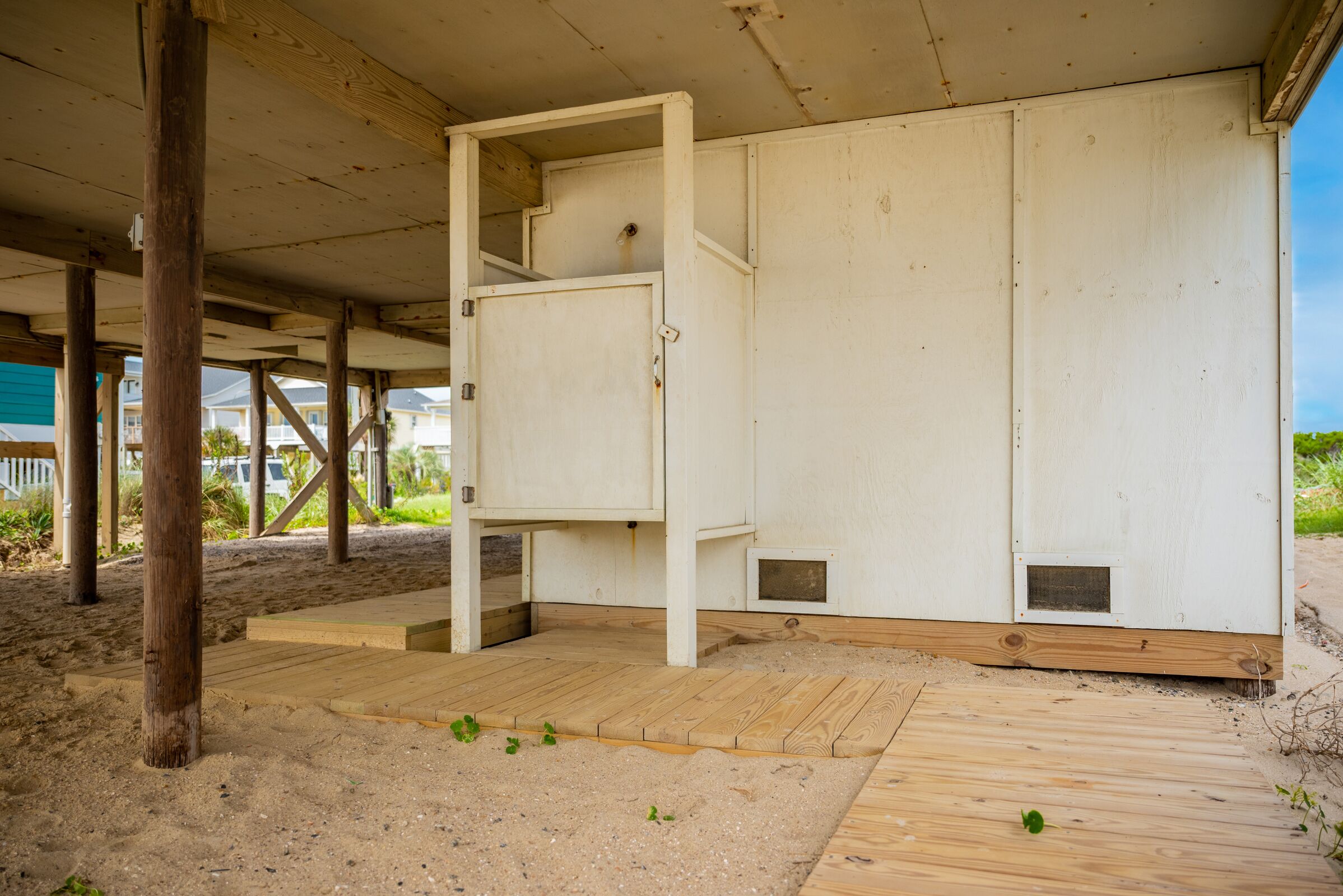 Ein Strandhaus mit einer Holzterrasse, einem Sandboden und einer weißen Fassade.