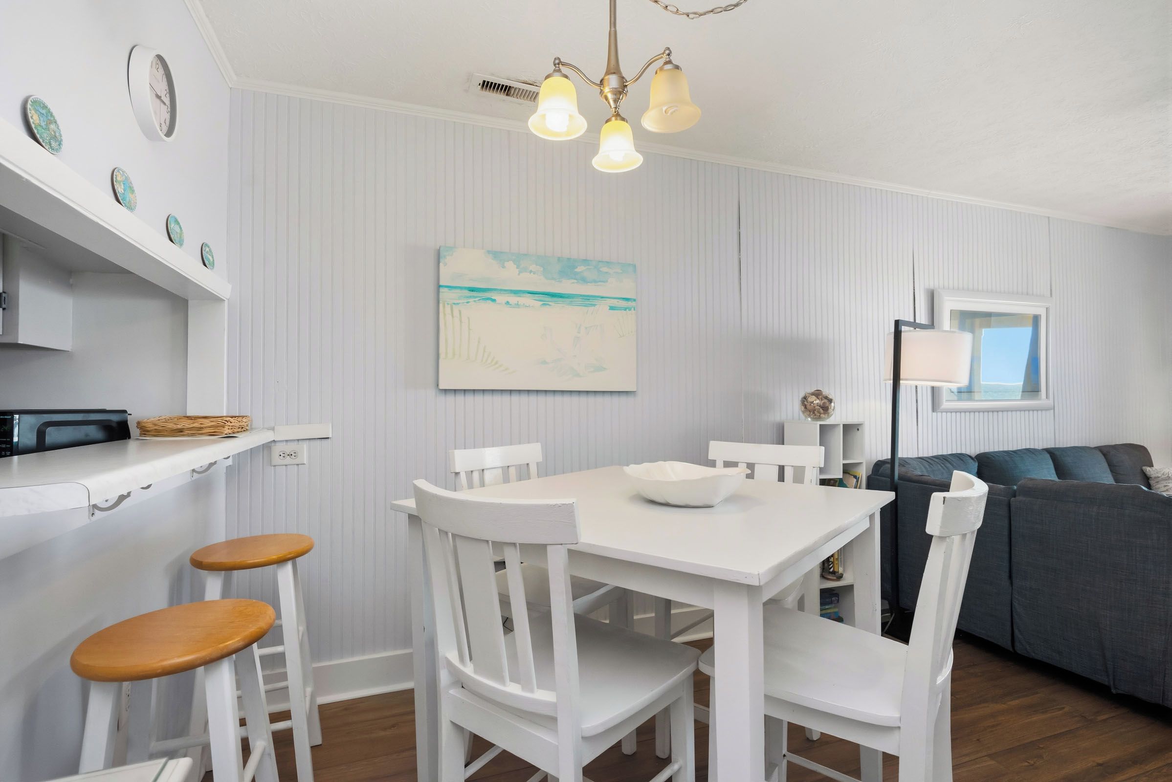 Een moderne keuken met witte kastjes, een eettafel met stoelen, een magnetron en een hangende lamp.