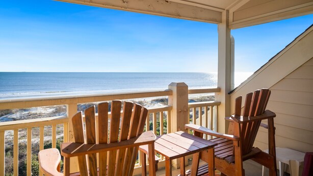 Un terrazzo in legno con due poltrone Adirondack e un tavolino, con vista su una spiaggia e l'oceano.