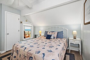 A bedroom with a bed, two bedside tables, a window with a view, and a door. - A Dream Come True: Oceanfront Condo with Community Pool (Caswell Beach)