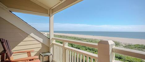 A covered balcony with a view of a beach and ocean.