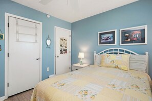 A bedroom with a bed, a nightstand, a wall-mounted shelf, and two framed pictures.