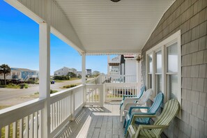 A covered porch with white railings and a view of the beach and houses in the background.