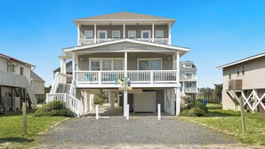 Ein zweigeschossiges Strandhaus mit Balkon, überdachter Auffahrt und kleiner Veranda.