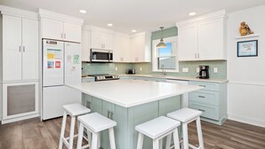 A modern kitchen with white cabinets, a large island with bar stools, a microwave, and a coffee maker. - Linger Longer: Oceanfront with Great Views of Lighthouse (Caswell Beach)