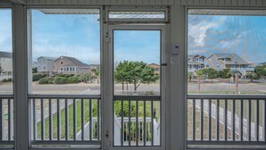 En vy från en veranda med ett vitt räcke, med utsikt över en gata med hus och ett träd.