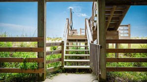 Una escalera de madera que sube a un nivel superior, rodeada de barandillas de madera y con vistas despejadas a la playa.