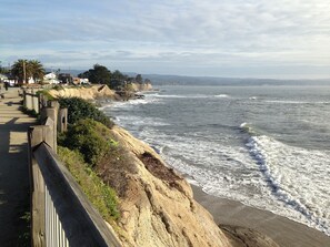 A coastal walkway with a wooden railing, leading to a sandy beach with waves crashing onto the shore. - Pleasure Point Oasis ~ Family and dog-friendly yard ~ Off-street parking (Santa Cruz)