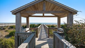 A wooden boardwalk leading to a gazebo with a view of the beach and ocean.