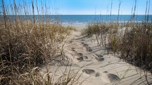 A sandy beach path with footprints leading to the ocean, surrounded by tall grass.