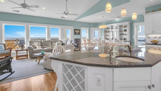 A spacious living area with a large window, a ceiling fan, and a kitchen with white cabinets and a granite countertop.