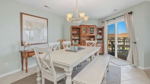 A dining area with a white table, chairs, and a chandelier. There is a large window with a view of a building outside.