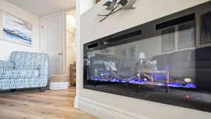 A living room with a fireplace, a sofa, and a patterned armchair. - By The Ocean Blue: Oceanfront Luxury on Caswell Beach with Community Pool (Caswell Beach)