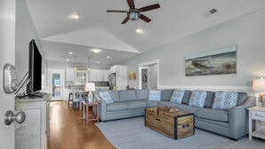 A modern living room with a grey sectional sofa, wooden coffee table, and a painting of a boat on the wall. - All Summer Long: Modern Home located in the Woodlands and Waterway area of Oak I (Oak Island)
