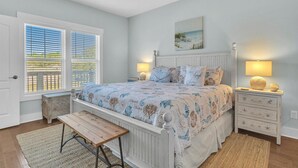 A bedroom with a bed, bedside lamps, a bench, a window with blinds, and a ceiling fan. - All Summer Long: Modern Home located in the Woodlands and Waterway area of Oak I (Oak Island)