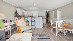 A spacious living room with a dining area, kitchen, and a ceiling fan. - OW 4101: Serene Condo with Community Pool, Elevator (Oak Island)