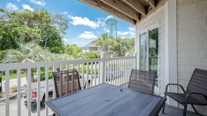 A covered outdoor area with a table and chairs, a white fence, and a view of a water tower and trees. - OW 4101: Serene Condo with Community Pool, Elevator (Oak Island)