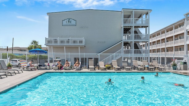 A swimming pool area with a building labeled "CW Condominiums" in the background. - OW 4101: Serene Condo with Community Pool, Elevator (Oak Island)