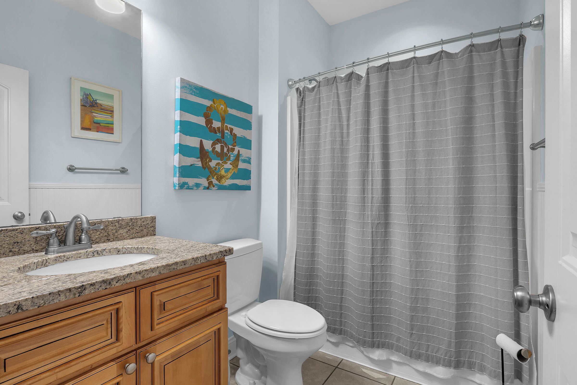 A bathroom with a granite countertop sink, wooden cabinets, a white toilet, and a shower curtain.