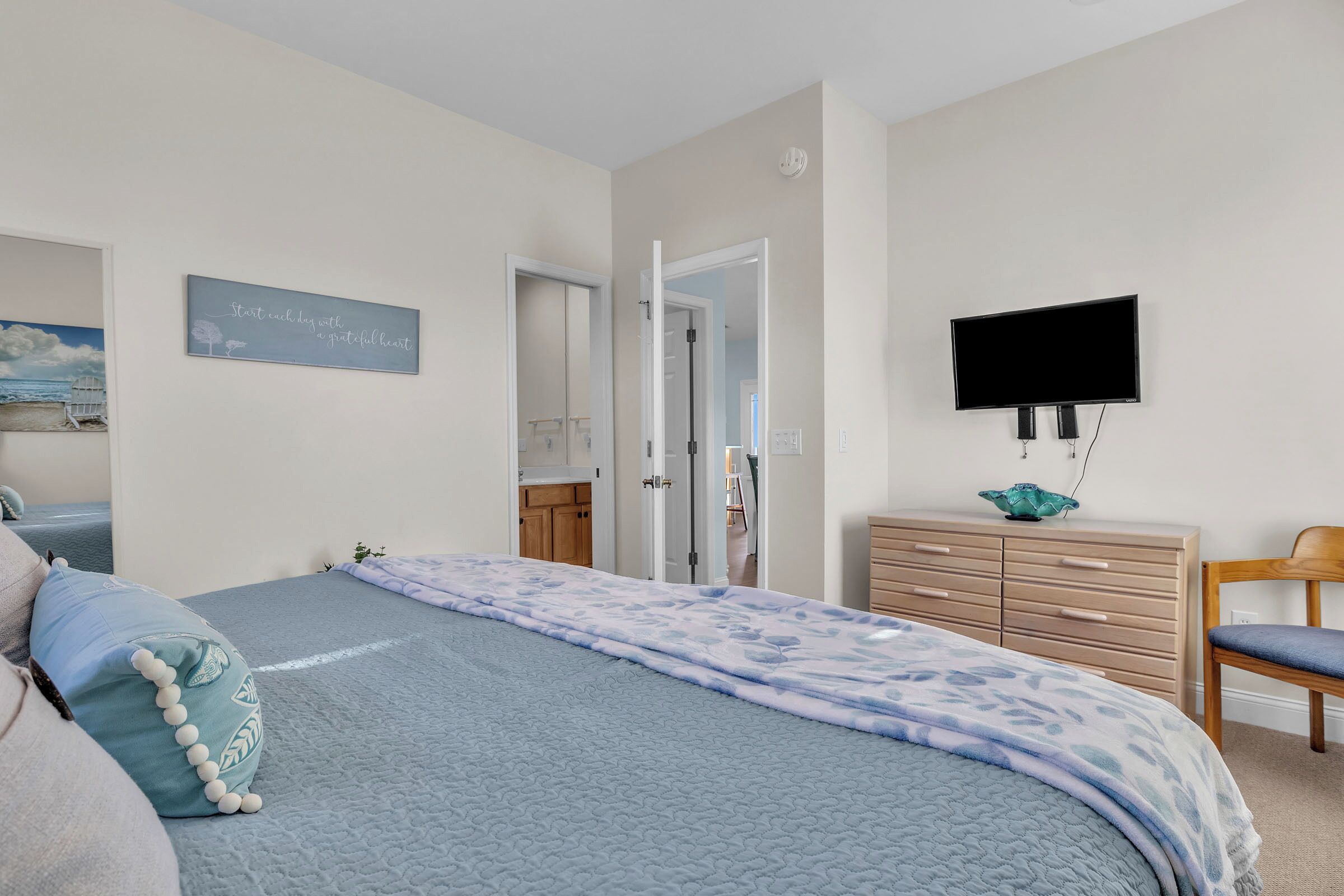 Een slaapkamer met een bed, een dressoir, een televisie en een deur naar een badkamer.