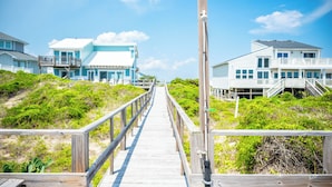 A wooden boardwalk leading to beachfront houses with balconies and railings. - Beach Buzz: Oceanfront with Expansive Beach and Sound Side Decks (Caswell Beach)