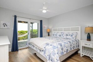 Ein Schlafzimmer mit einem Bett, zwei Nachttischen, einem Deckenventilator und Blick auf Grün durch eine Schiebetür.