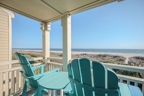 Une véranda abritée avec deux fauteuils Adirondack turquoise et une table, donnant sur une plage.