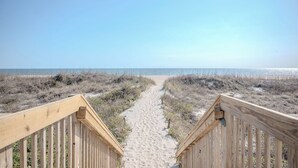 Ein hölzerner Weg führt zu einem Strand unter einem wolkenlosen Himmel.