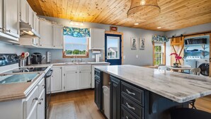 Una cocina moderna con armarios blancos, una isla grande y techo de madera.