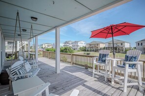 Una terraza techada con muebles blancos, un paraguas rojo y vista a casas al fondo.