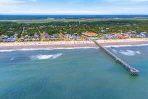 Une vue aérienne d’une zone côtière, avec une jetée qui s’avance dans l’eau, entourée de bâtiments résidentiels et d’une plage.