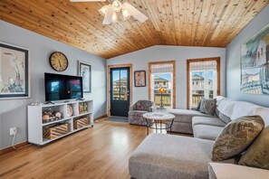 Un salon avec un plafond en bois, un téléviseur, un canapé, une table basse et une porte donnant sur l’extérieur.