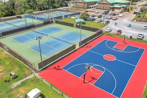 Un terrain multisports doté de courts de tennis et de basketball, entouré d’un parking et avec un bâtiment en arrière-plan.