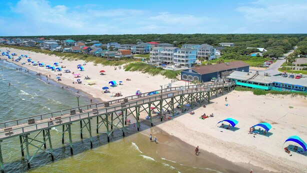 Una playa con un muelle, sombrillas y casas de playa.