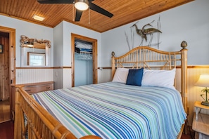 Un dormitorio con cama de madera, mesita de noche, espejo y ventilador de techo.