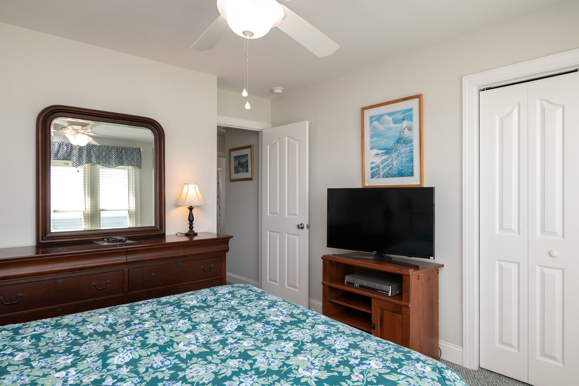 Une chambre à coucher avec un lit, une commode, un téléviseur et un ventilateur de plafond.