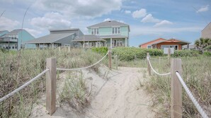Un sendero arenoso que conduce a casas de playa con valla de madera y barrera de cuerda.