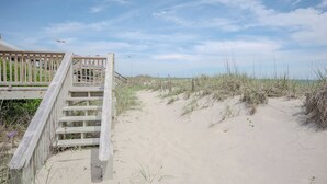 Una escalera de madera que conduce a una zona de playa con arena y dunas.