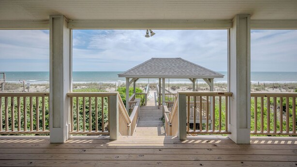 Una terraza de madera que conduce a un pabellón con vistas a la playa y al océano.