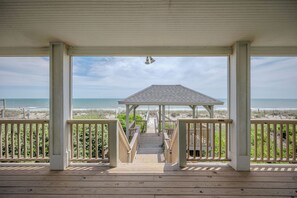 Una terraza de madera que conduce a un pabellón con vistas a la playa y al océano.