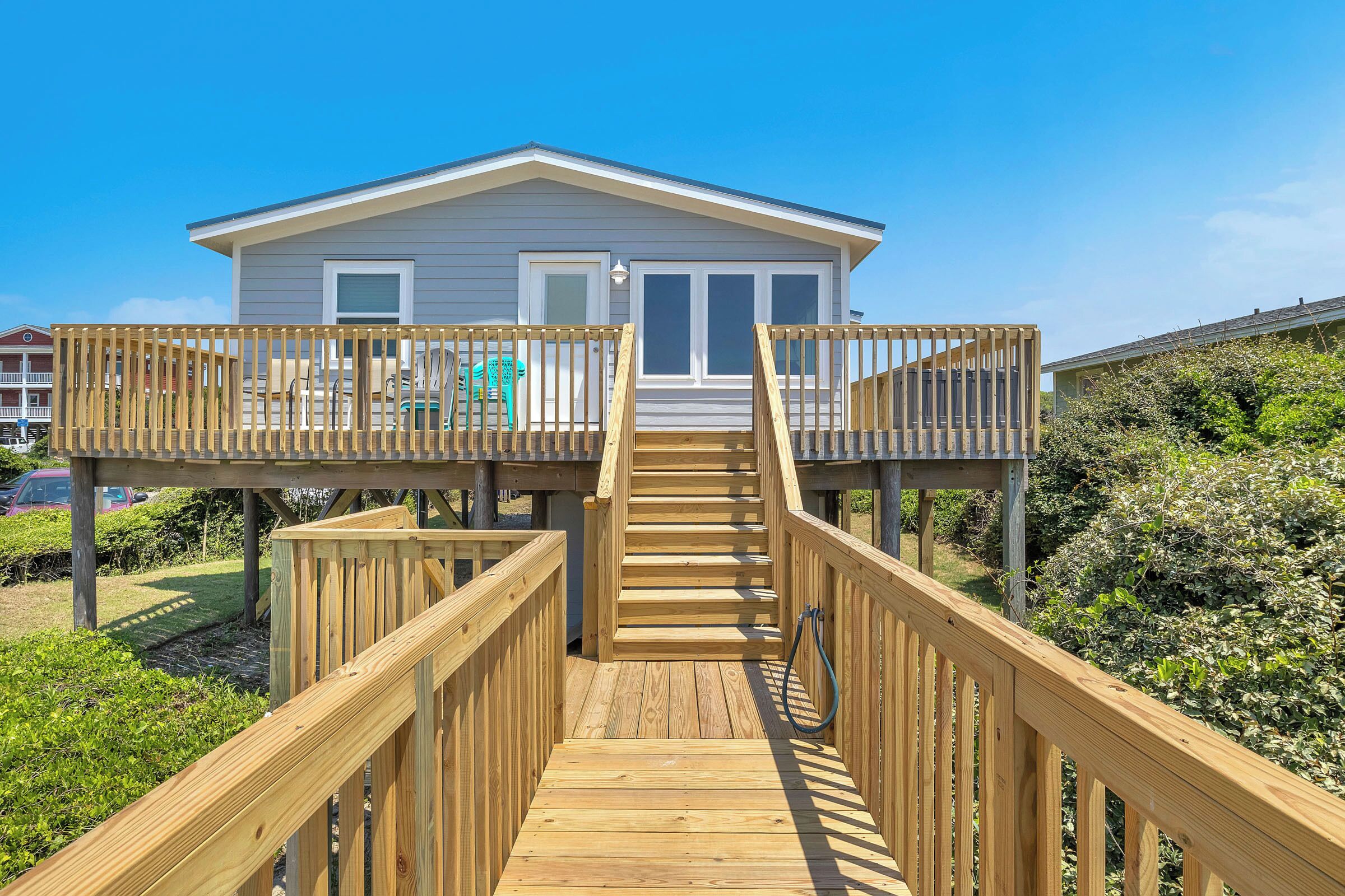 Une terrasse en bois menant à une maison dotée d’un balcon, le tout entouré de verdure.