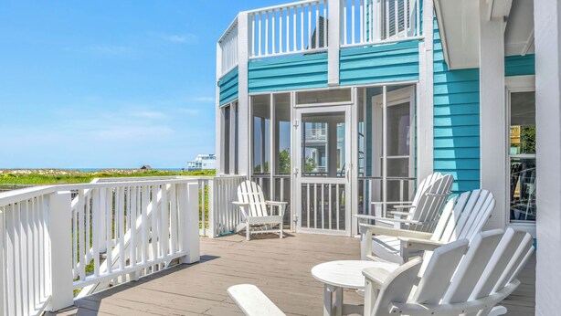 Une terrasse avec des chaises blanches et une table, donnant sur une plage.
