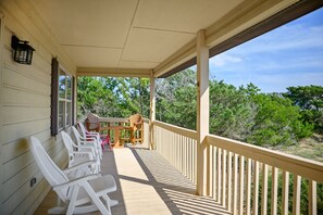 Eine überdachte Veranda mit weißen Plastikstühlen, einem Holztisch und Blick auf Bäume.