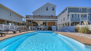 En swimmingpool med træterrasse og liggestole, omgivet af toetagers huse med balkoner.